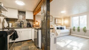 A compact living space with a kitchenette, a dining area, and a bedroom with a large window.