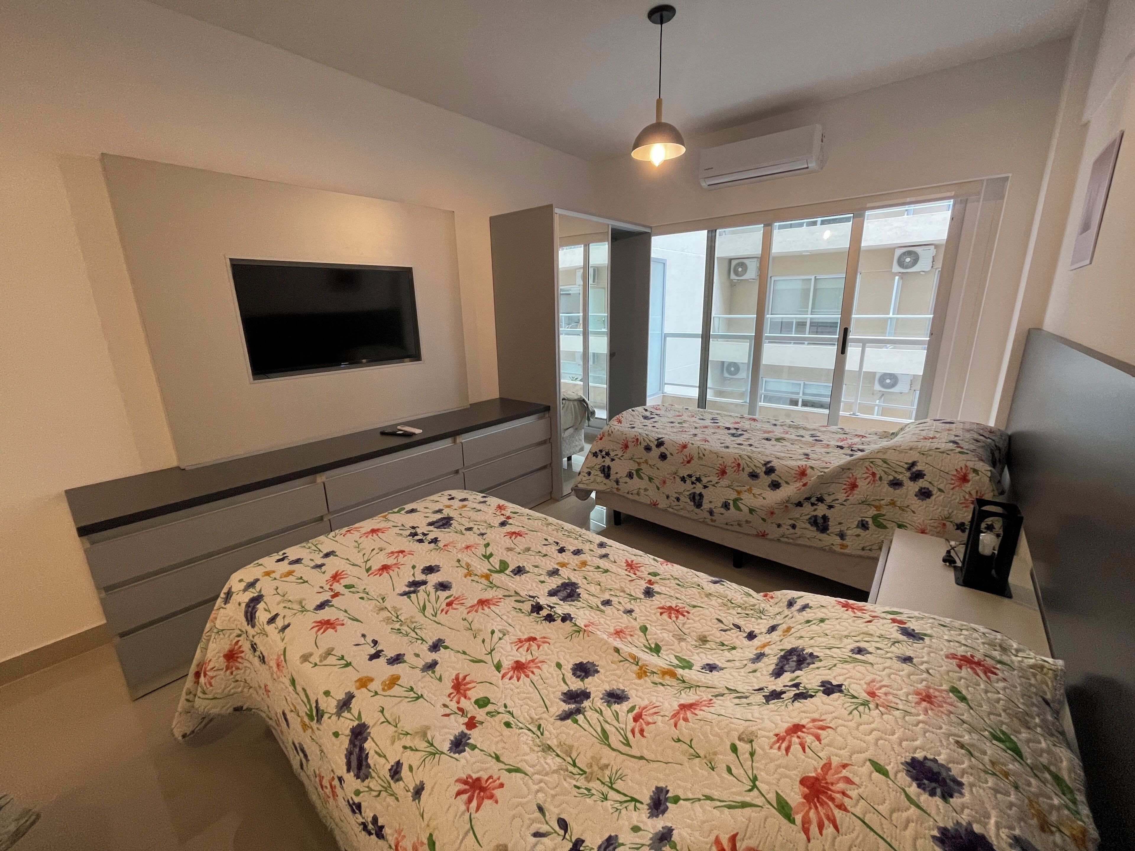 A bedroom with two beds, a TV, and a window with a view of buildings.