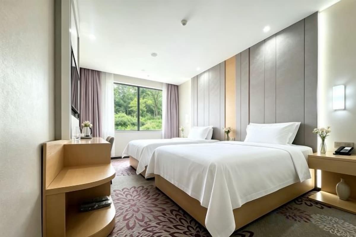 A hotel room with a large bed, a desk, and a view of greenery outside.