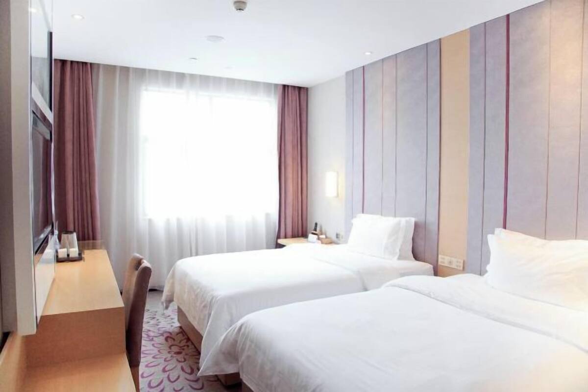 A hotel room with two beds, a desk, and a large window with curtains.