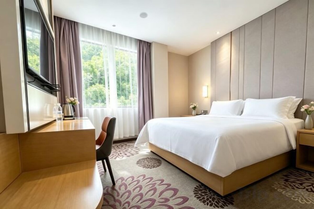 A hotel room with a bed, a desk, a chair, and a window with curtains.