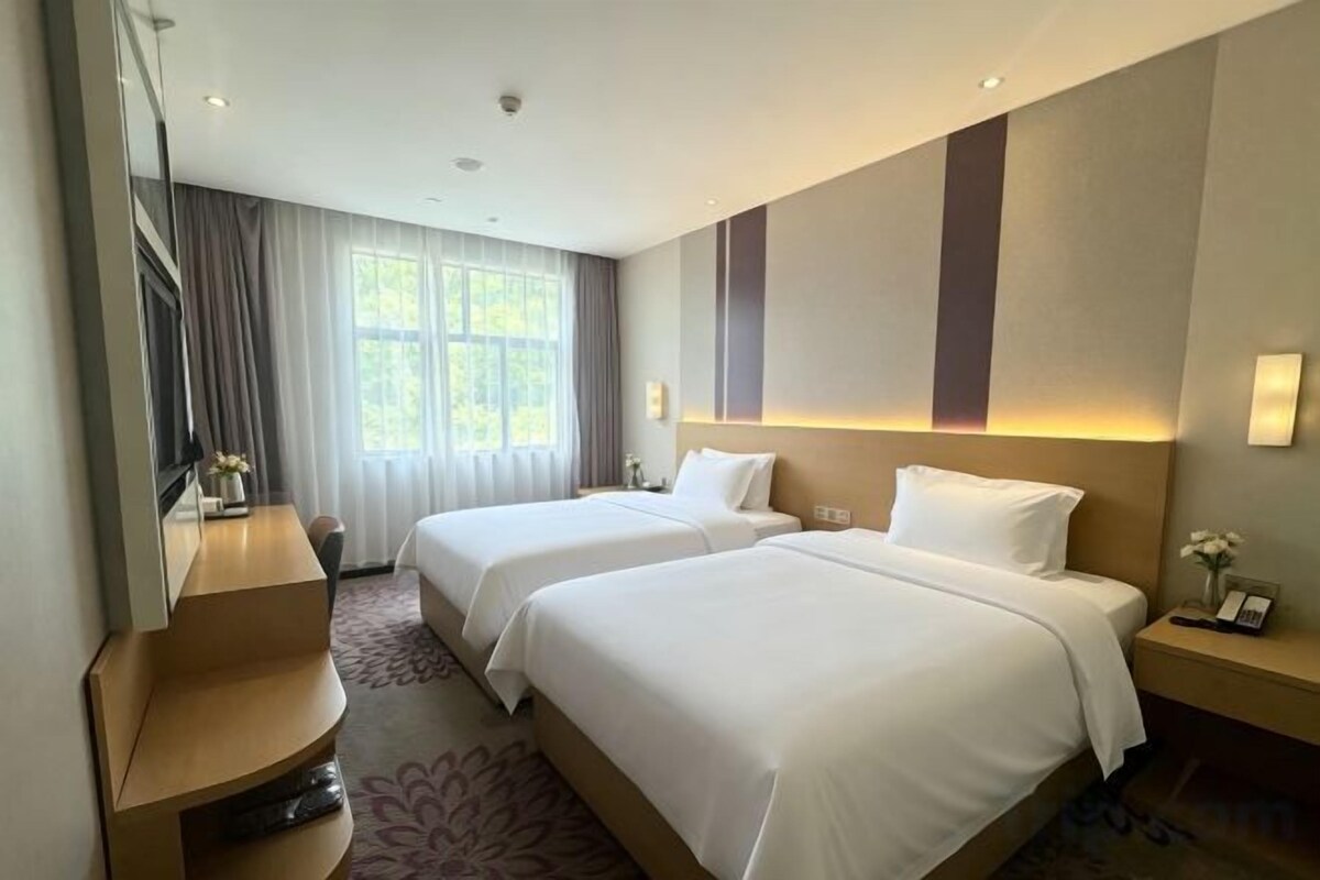 A hotel room with two beds, a desk, and a large window with curtains.
