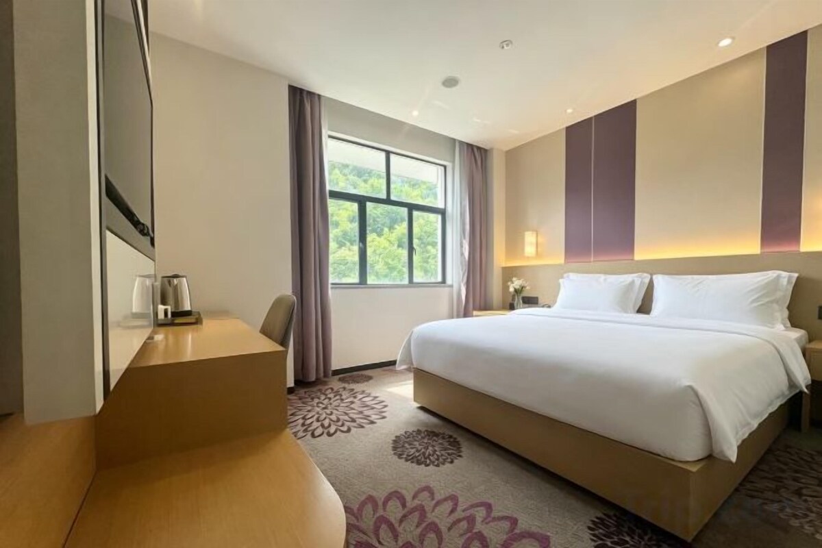 A hotel room with a bed, a desk, a chair, a window with curtains, and a patterned rug.