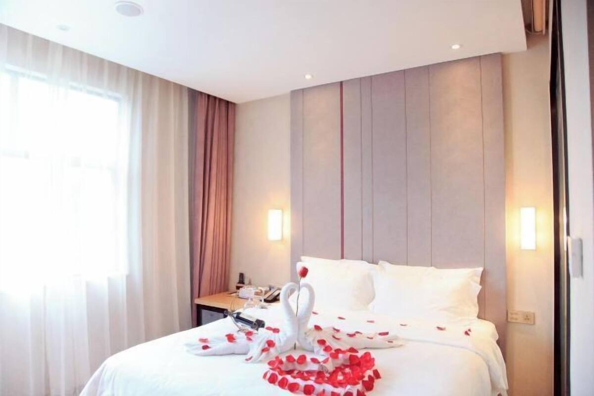 A hotel room with a bed, a bedside table, and a window with curtains.