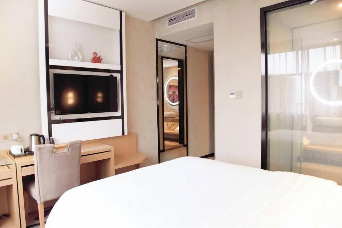 A hotel room with a bed, a desk, a chair, a mirror, and a vanity with a circular mirror.