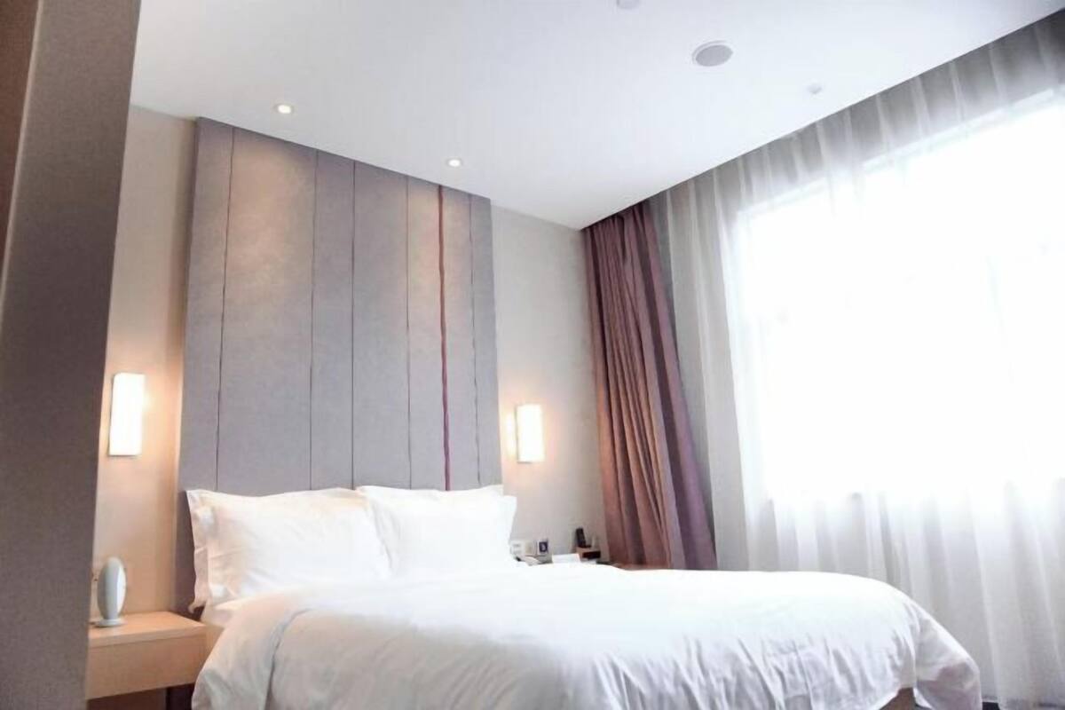 A hotel room with a bed, nightstands, and a large window with curtains.