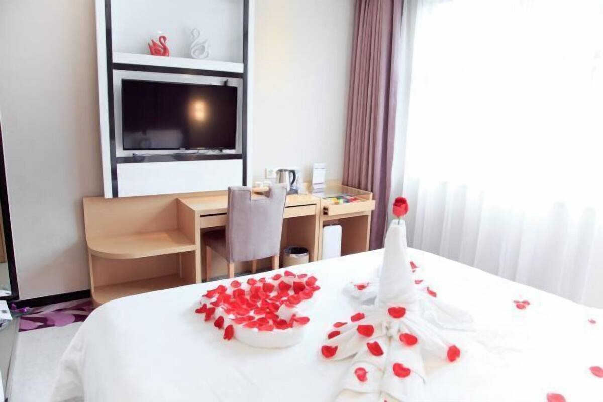 A hotel room with a bed, a desk, a chair, a television, and a window with curtains.