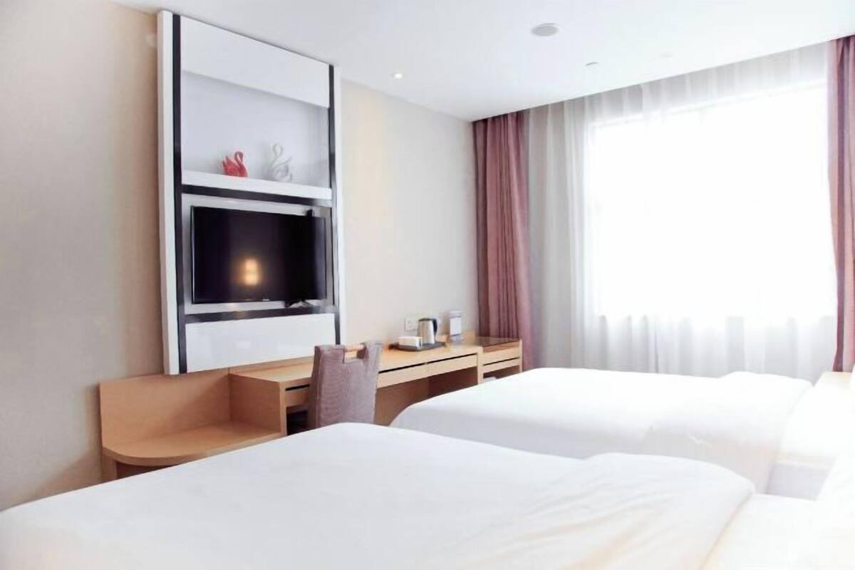 A hotel room with two beds, a TV, a desk, and a window with curtains.