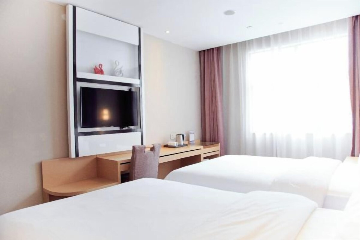 A hotel room with two beds, a TV, a desk, and a window with curtains.