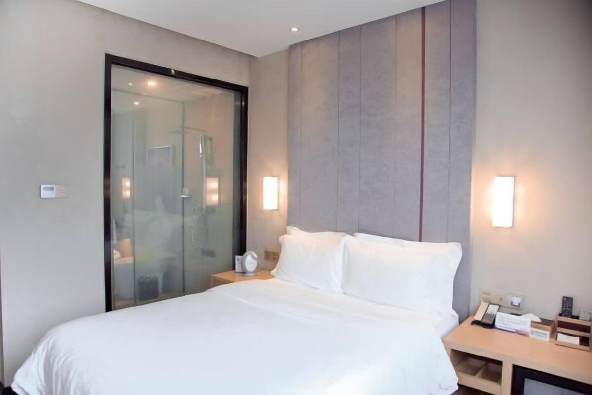 A modern hotel room with a large bed, a glass shower enclosure, and bedside lamps.