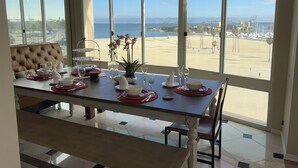 Una mesa de comedor dispuesta con platos, vasos y un florero, con vista a la playa.