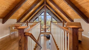 A high-ceilinged attic room with wooden beams, a staircase, and a view of the outdoors. - Best Mountain Views in Estes! Large Family Home (Estes Park)