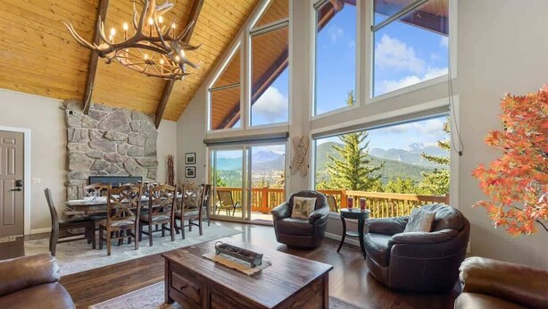 A spacious living room with a stone fireplace, large windows offering mountain views, and a cozy seating area. - Best Mountain Views in Estes! Large Family Home (Estes Park)