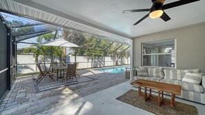 A covered patio with a pool, a wooden table, and a sofa. - Endless Summer Escape Near SK (Sarasota)