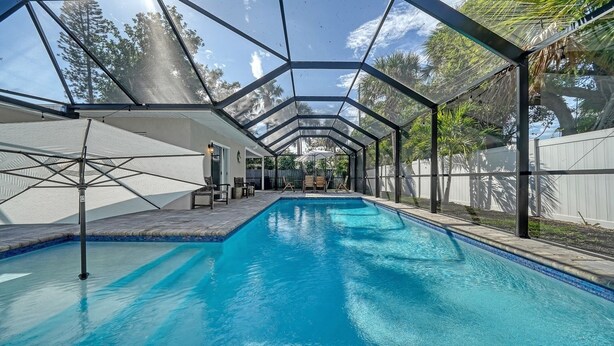A swimming pool with a covered area, surrounded by a fence and trees. - Endless Summer Escape Near SK (Sarasota)