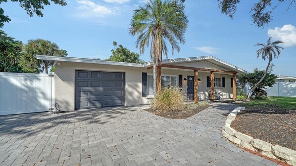 A single-story house with a garage, a covered porch, and a landscaped front yard with palm trees and shrubs. - Endless Summer Escape Near SK (Sarasota)