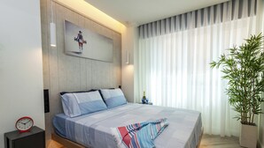 A modern bedroom with a bed, a nightstand, a wall-mounted clock, a painting, and a potted plant.