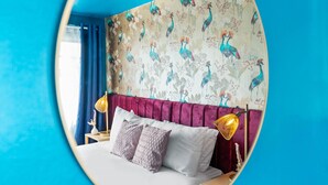 Quarto com cama, duas luminárias de cabeceira, espelho e parede com padrão de pássaros.