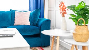 Uma sala de estar moderna com um sofá azul, uma mesa de centro branca e uma pequena mesa branca com um vaso e planta.