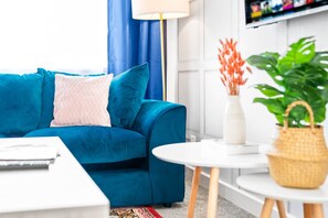 A modern living room with a blue sofa, a white coffee table, and a small white table with a vase and plant. - Stylish 3 Bedroom House - Parking - Garden (Birmingham)