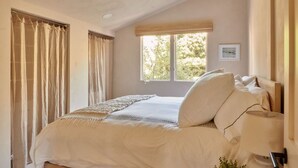 Un dormitorio con cama, cortinas, una ventana y una lámpara fijada a la pared.