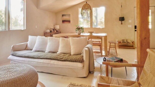 Un salón amplio con sofá, reposapiés y sillas de mimbre. En el fondo, una mesa de comedor y sillas.