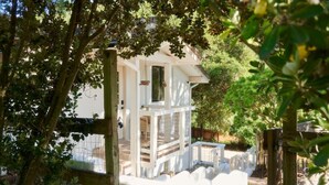 Un edificio blanco con balcón, rodeado de árboles y una valla de madera.