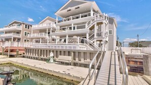 Une propriété en bord de mer, composée de plusieurs étages, dotée de balcons, d’une piscine et d’une terrasse en bois.