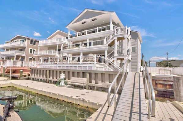 Une propriété en bord de mer, composée de plusieurs étages, dotée de balcons, d’une piscine et d’une terrasse en bois.