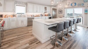 Une cuisine moderne avec des meubles blancs, un grand îlot central doté de tabourets et des luminaires suspendus.