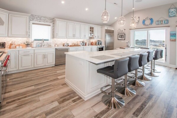 A modern kitchen with white cabinetry, a large island with bar stools, and pendant lighting.