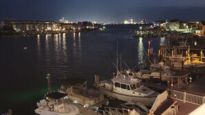 Un port de plaisance de nuit, avec des bateaux amarrés, un quai illuminé et, au loin, une vue sur les gratte-ciel de la ville.