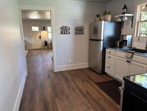 A modern kitchen with a stainless steel refrigerator, white cabinets, and a wooden floor. There are potted plants on the countertop and a coffee maker on the counter.