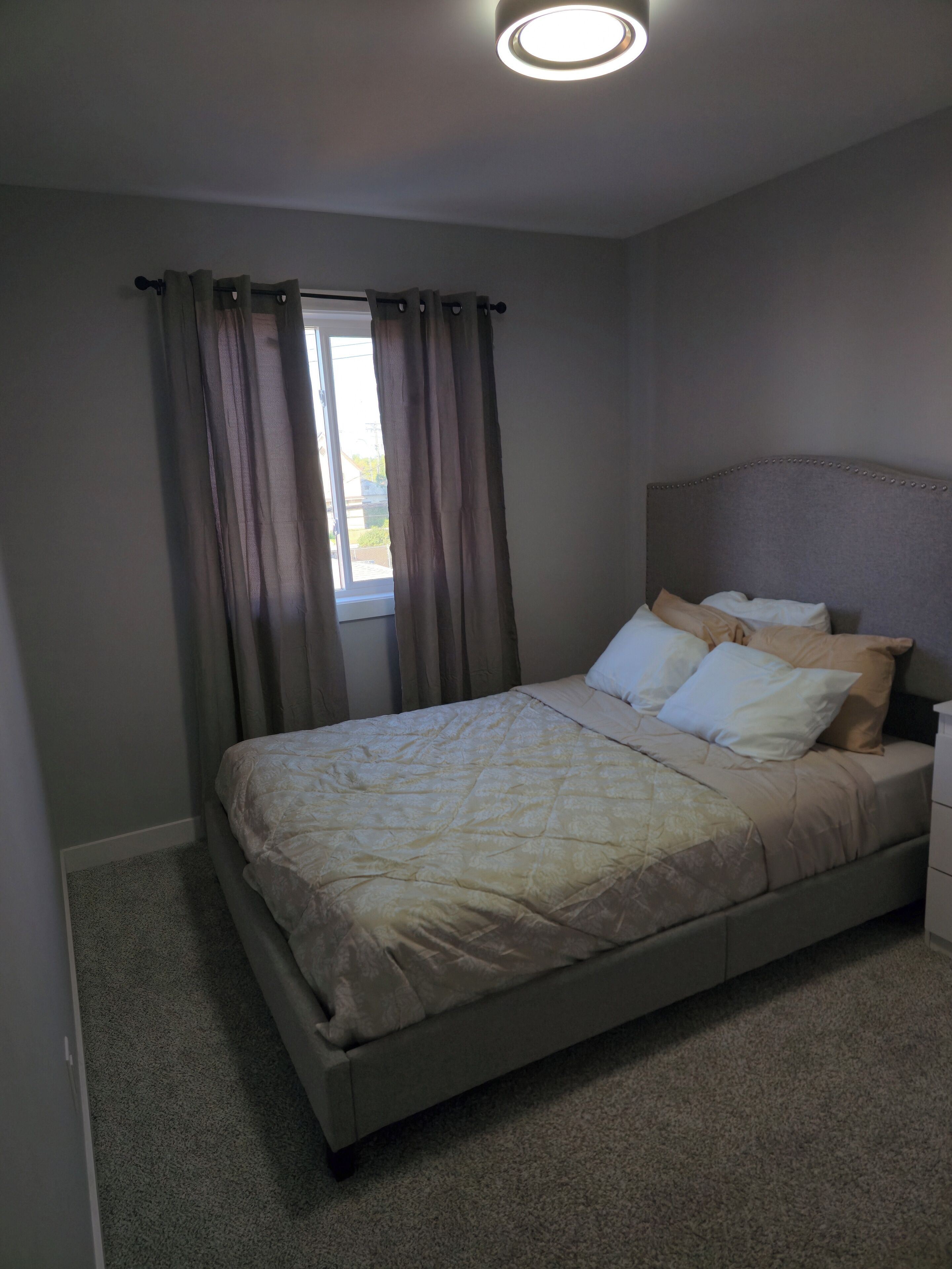 Ein Schlafzimmer mit Bett, Vorhängen, Nachttisch und Deckenleuchte.