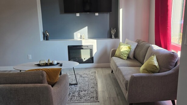 Una sala de estar moderna con una televisión de pantalla plana montada en la pared, un sofá, una mesa de centro y una chimenea.