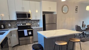 Una cocina moderna con armarios blancos, electrodomésticos de acero inoxidable y una isla central con taburetes.