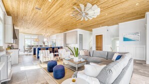 Un'ampia zona giorno con soffitto in legno, un divano grigio e un'area pranzo con un tavolo grande e sedie.