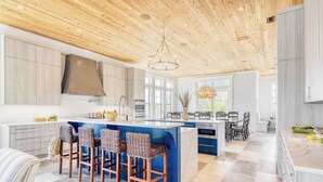 Una cucina moderna con isola centrale, sgabelli da bar e zona pranzo illuminata da un lampadario.
