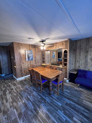 A dining area with a wooden table and chairs, a ceiling fan, and a blue sofa. - Beach and Launch Access (Mohave Valley)