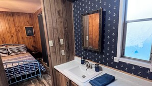 A compact room with wooden walls, a bed with striped bedding, a white sink, and a mirror above it. - Beach and Launch Access (Mohave Valley)