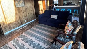 A spacious living area with a blue sofa, patterned cushions, and a striped rug. A ceiling fan and a world map artwork are visible. - Beach and Launch Access (Mohave Valley)