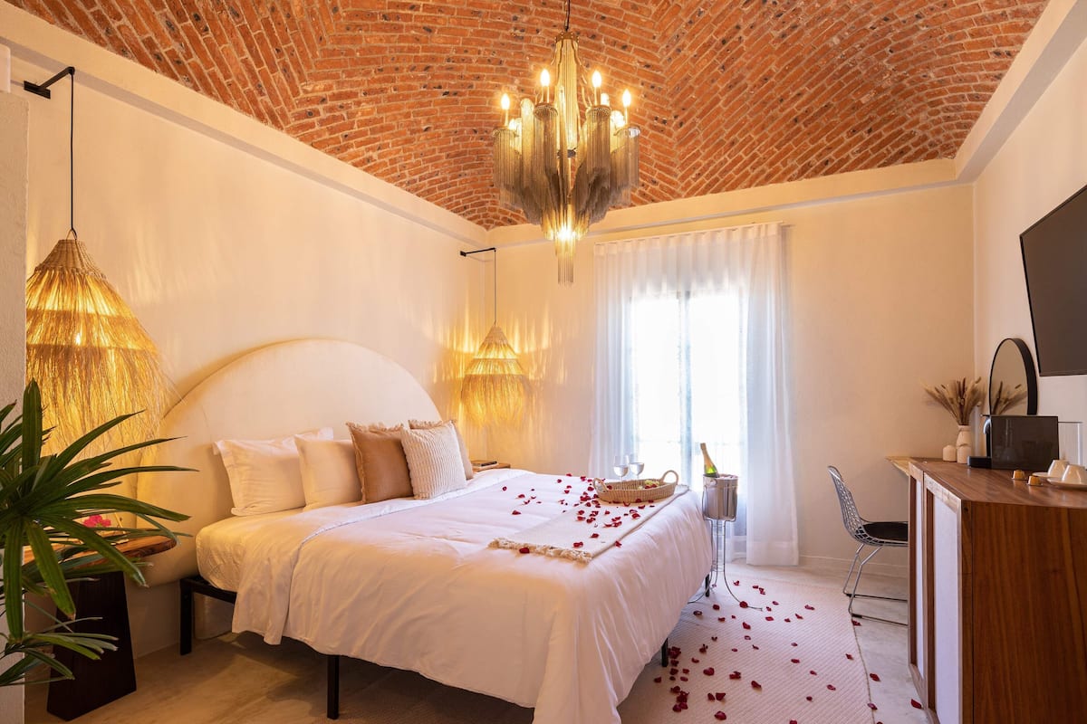 Ein geräumiges Schlafzimmer mit einem großen Bett, einer Chandelierleuchtre und einer Ziegeldecken.