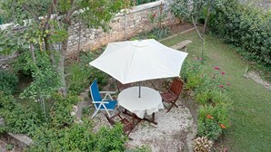 En terrasse med et rundt bord, stole, en parasol og krukker med planter.