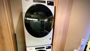 A compact laundry room with a front-loading washer and dryer stacked vertically. - Bear Mountain -Suite 8 (Grants Pass)