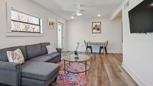 Una sala de estar con un sofá gris, una mesa de centro de cristal y una mesa de comedor de madera con sillas.