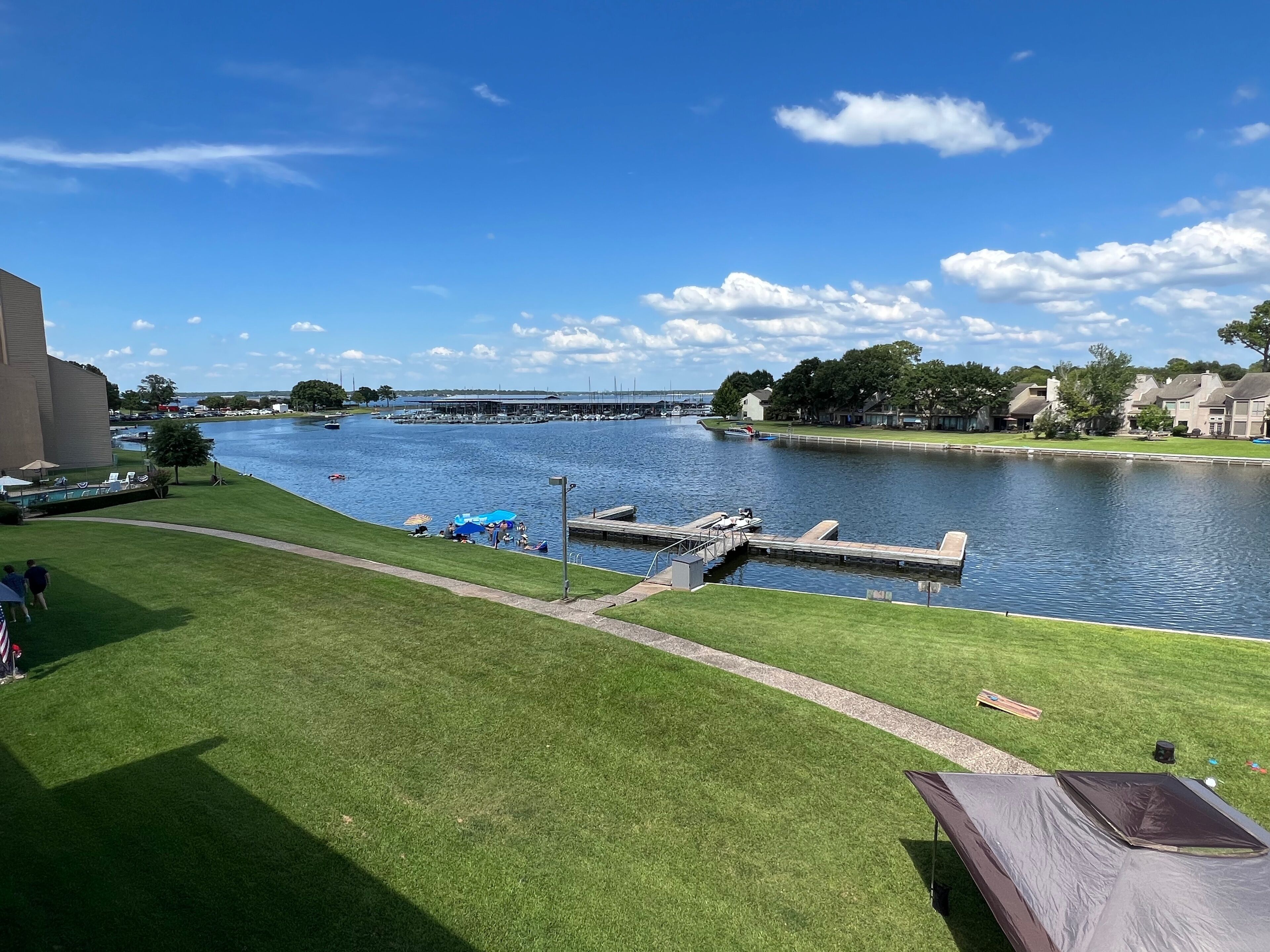A riverside view with a grassy area, a dock, and a building in the background.