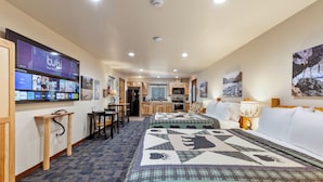 Habitación de hotel con una cama grande, televisión montada en la pared, kitchenette y zona de comedor.