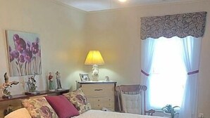 A bedroom with a bed, a nightstand, a lamp, a dresser, a window with curtains, and a ceiling fan. - 2 BR Entire Peaceful Home  (Trion)