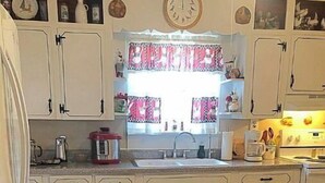 A kitchen with white cabinets, a sink, and a window with patterned curtains. - 2 BR Entire Peaceful Home  (Trion)