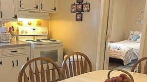 A dining area with a round table, wooden chairs, and a basket of apples. There is a kitchen with white cabinets and a stove in the background. - 2 BR Entire Peaceful Home  (Trion)